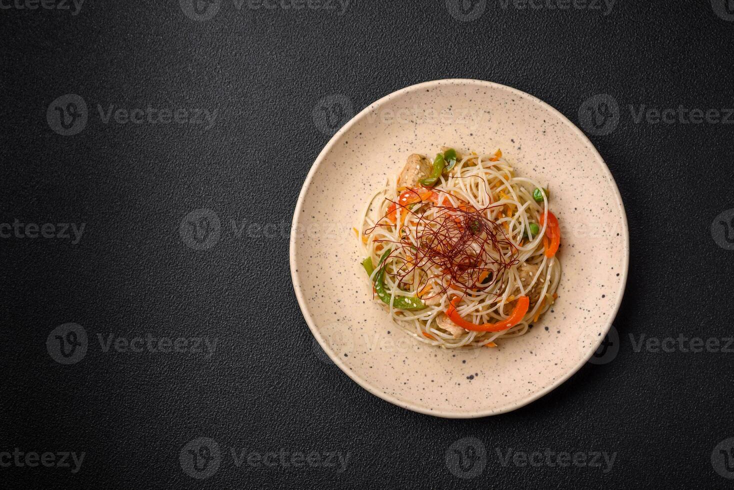 Tasty dish of Asian cuisine with rice noodles, chicken, asparagus, pepper, sesame seeds photo