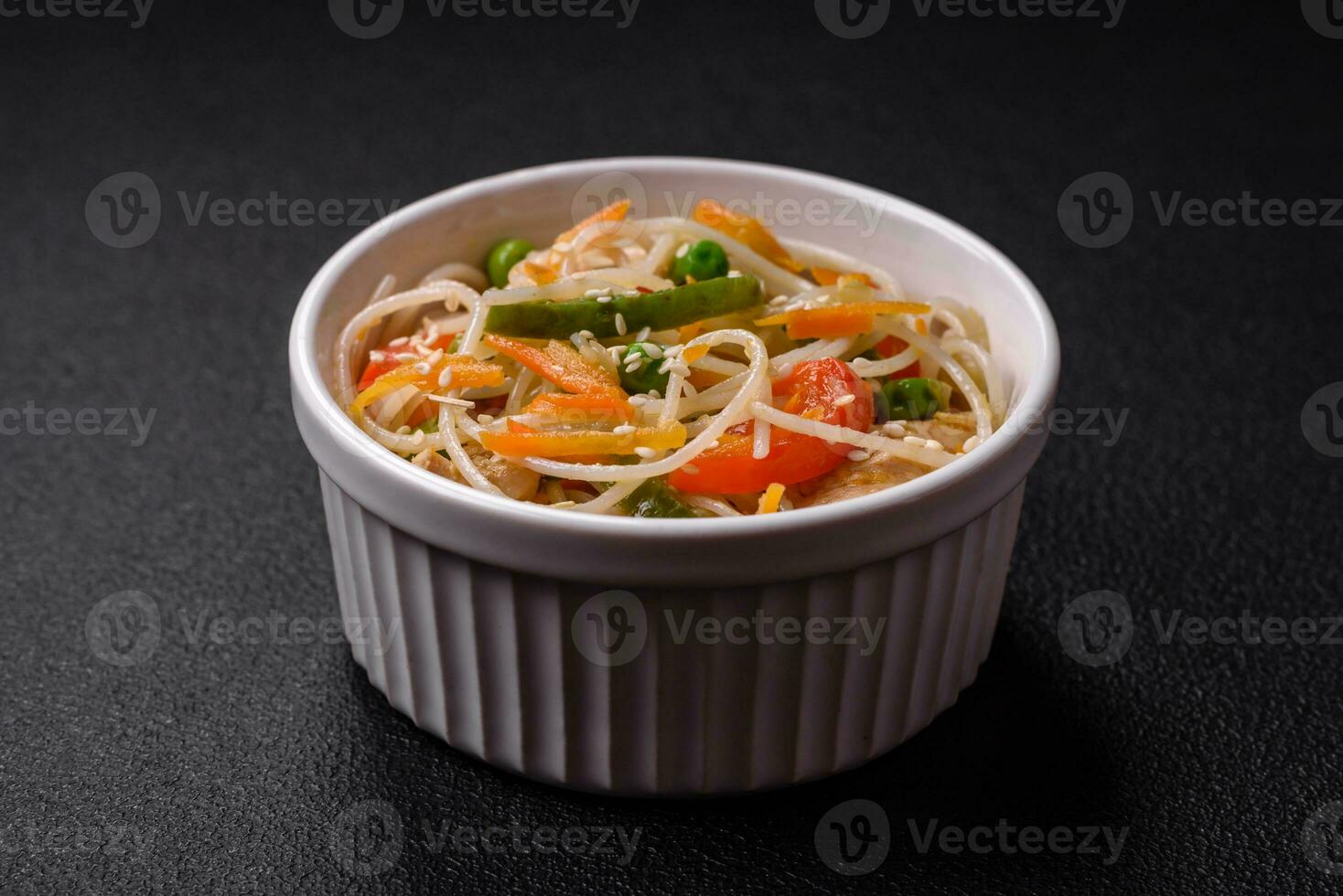 Tasty dish of Asian cuisine with rice noodles, chicken, asparagus, pepper, sesame seeds photo