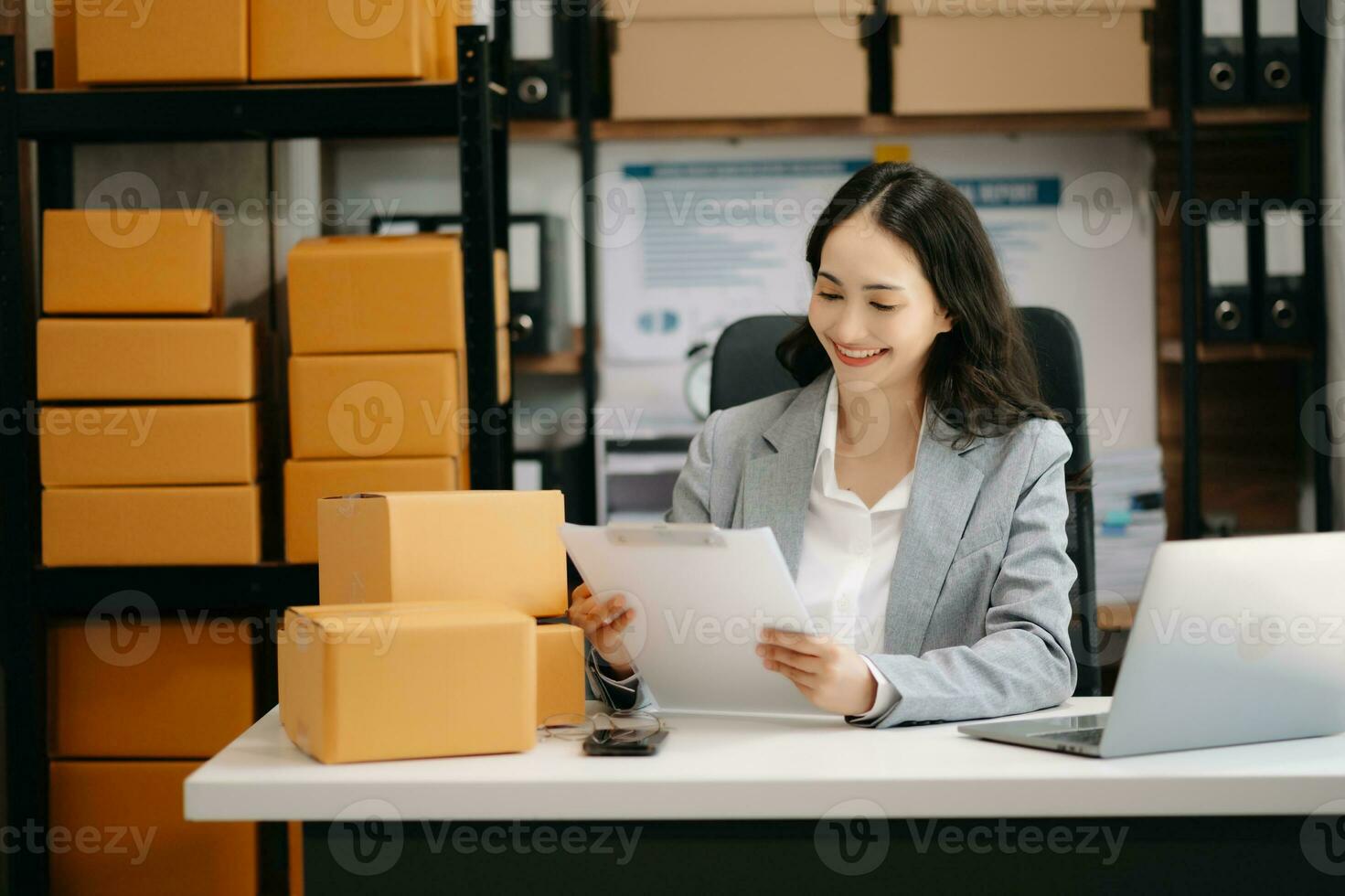 Startup small business SME, Entrepreneur owner woman using smartphone or tablet taking receive and checking online purchase shopping order to preparing pack product box. photo