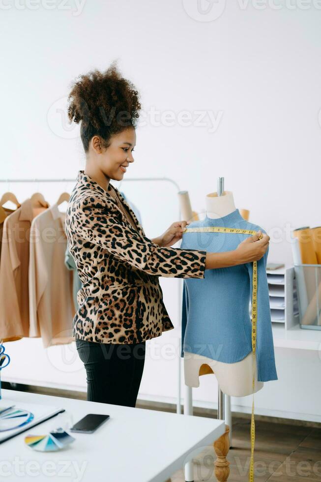 African tailor woman working on clothes in tailoring atelier. beautiful young female fashion designer smile and after success in studio photo