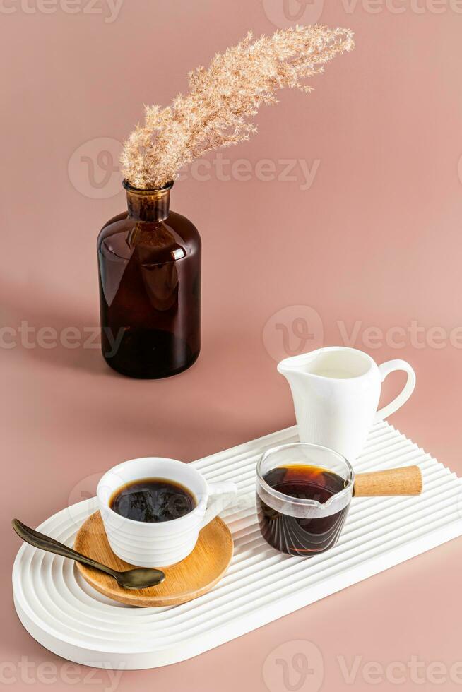 A small cup of freshly brewed espresso coffee on a white ceramic tray in the form of an. a vase with dry branches. Vertical view. photo