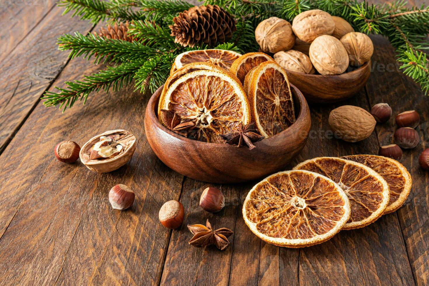 Two wooden bowls with dried orange slices and walnuts on a wooden table with spruce branches. Preparing Christmas decor in the village. photo