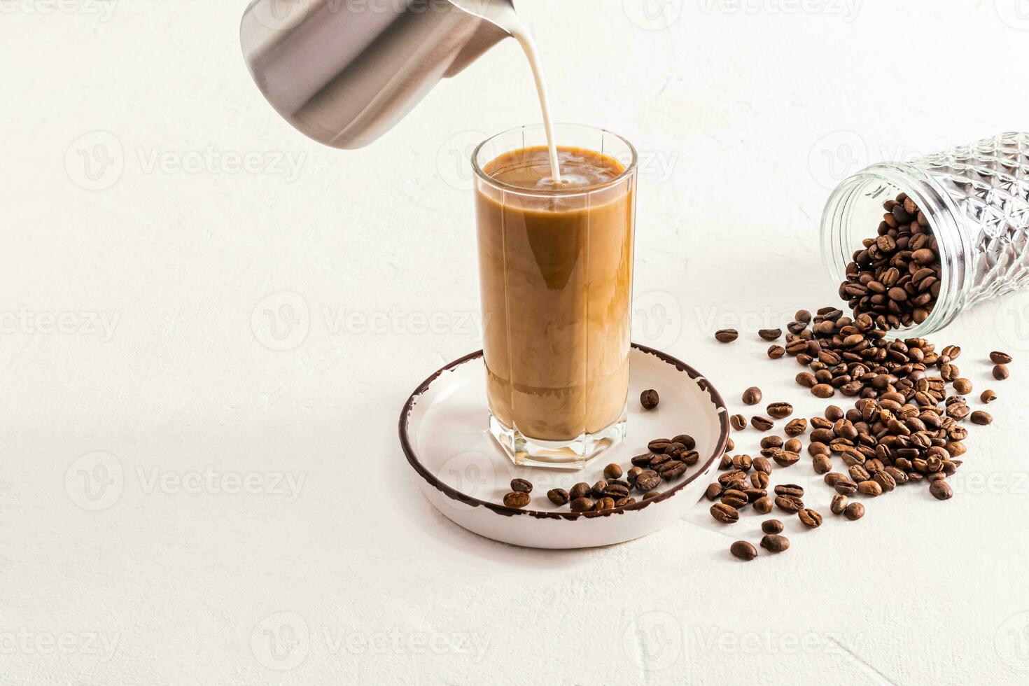 A stream of milk from a metal jug is poured into a high glass of ice-cold coffee. cans for storing coffee. Preparation of a delicious drink photo