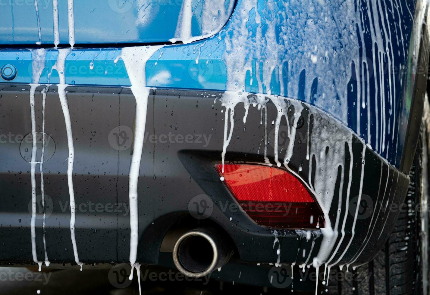 Blue car wash with white soap foam and professional auto care service. Car cleaning service concept. Vehicle cleaning service. Foam wash car detailing. Blue luxury SUV car is covered with white foam. photo