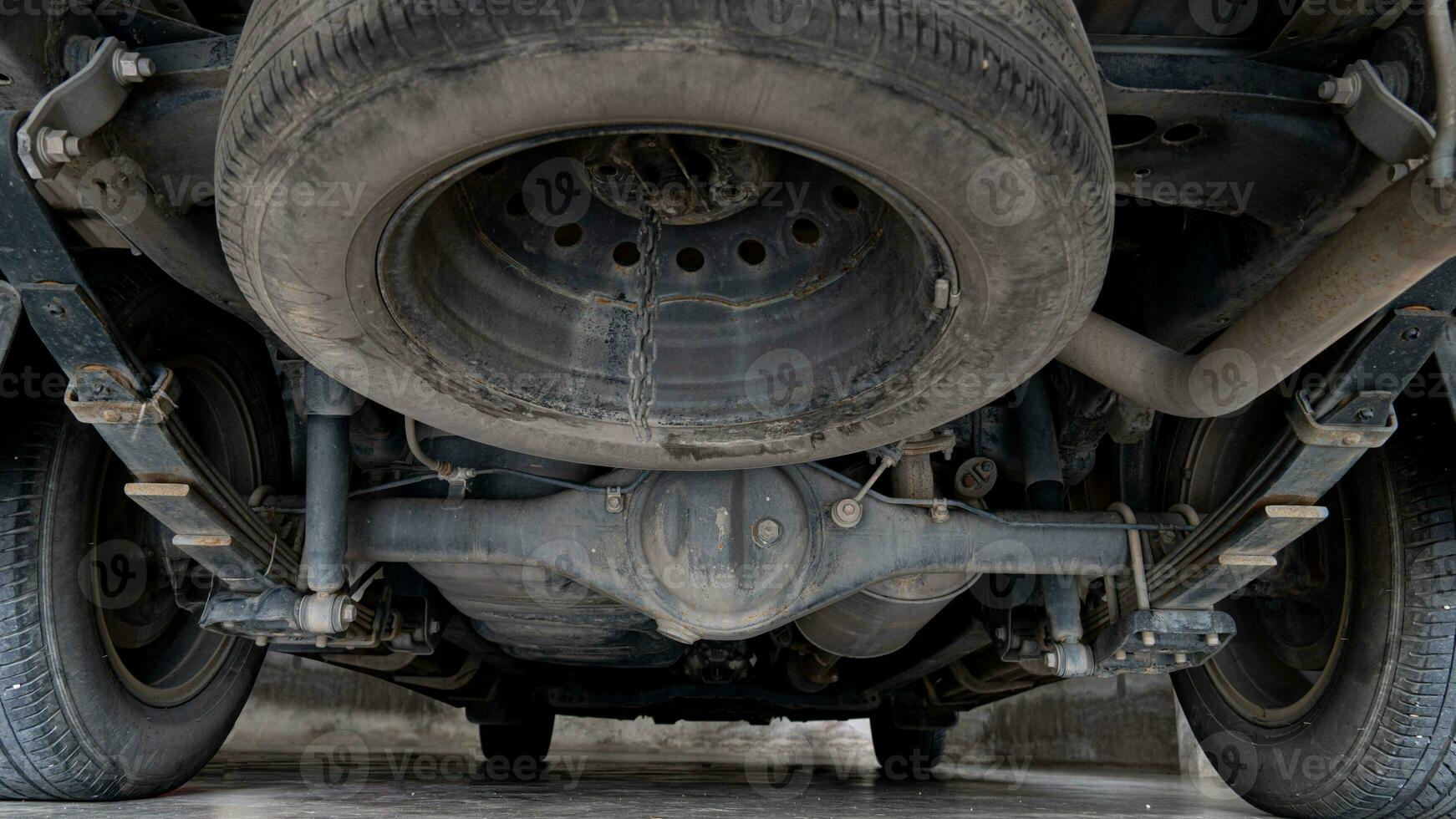 Maintenance background of car's suspension reveals the rear drive shaft. Cars parked on the cement floor. photo