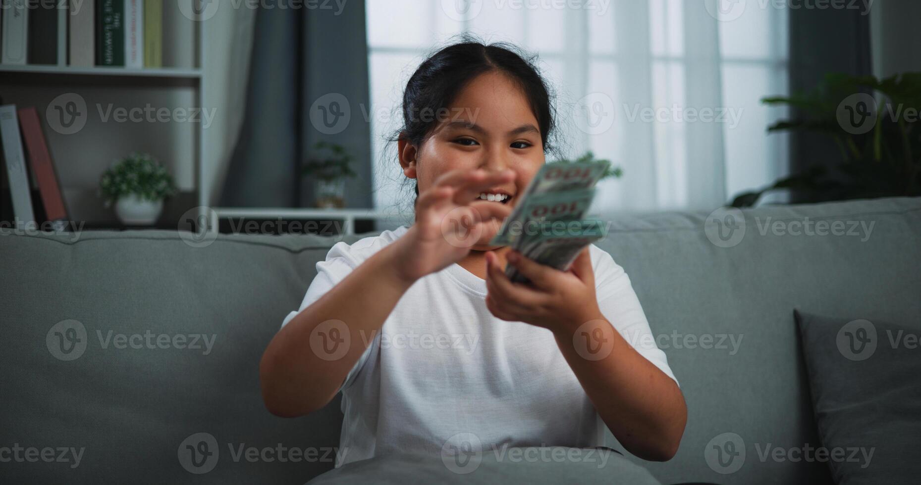 Portrait of a young Asian woman enjoying scattering cash bills on a sofa in the living room at home. photo