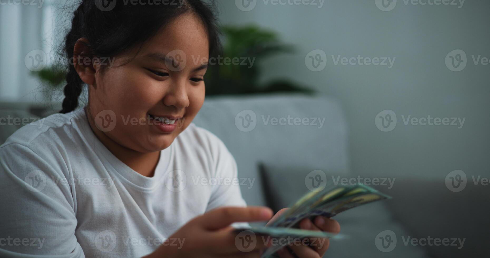 Portrait of young Asian woman enjoy counting cash dollars banknotes on sofa in the living room at home. photo