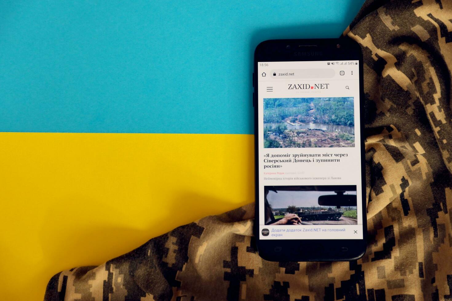 KYIV, UKRAINE - 4 MAY, 2023 Zaxid Net ukrainian news portal on smartphone screen with ukrainian flag and camouflage fabric photo
