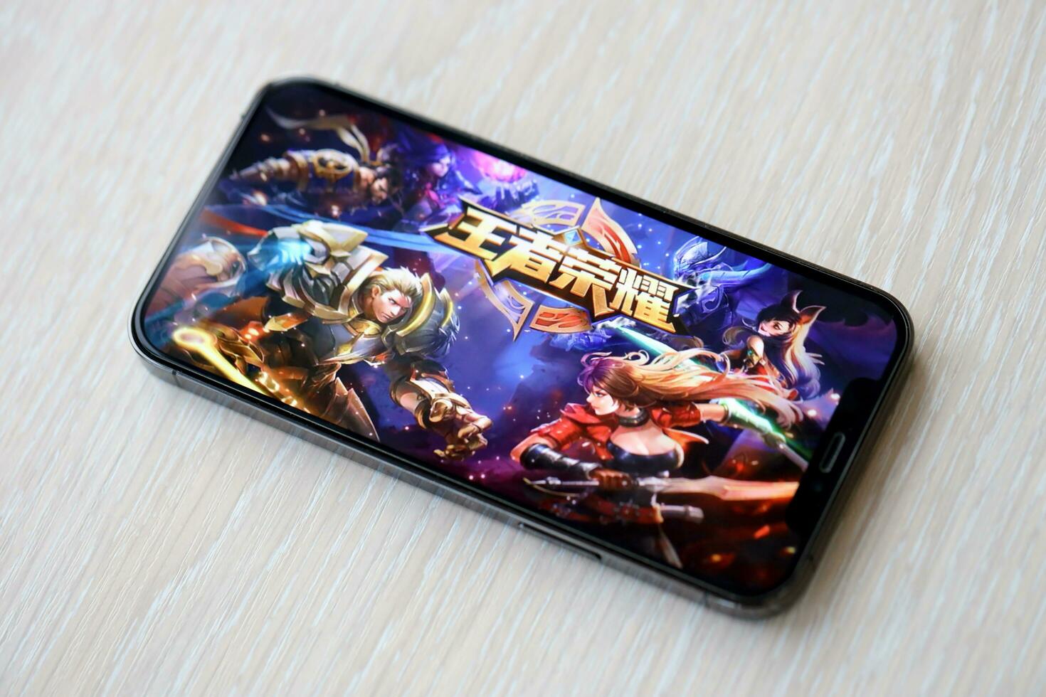 Honor of Kings mobile iOS game on iPhone 15 smartphone screen on wooden table during mobile gameplay photo