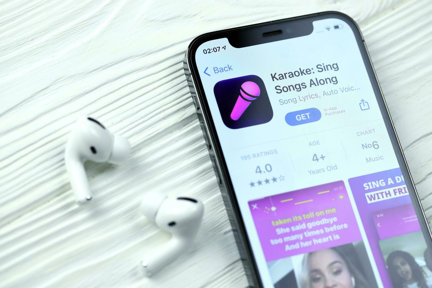 KHARKOV, UKRAINE - MARCH 5, 2021 Karaoke icon and application from App store on iPhone 12 pro display screen with airpods pro on white table photo