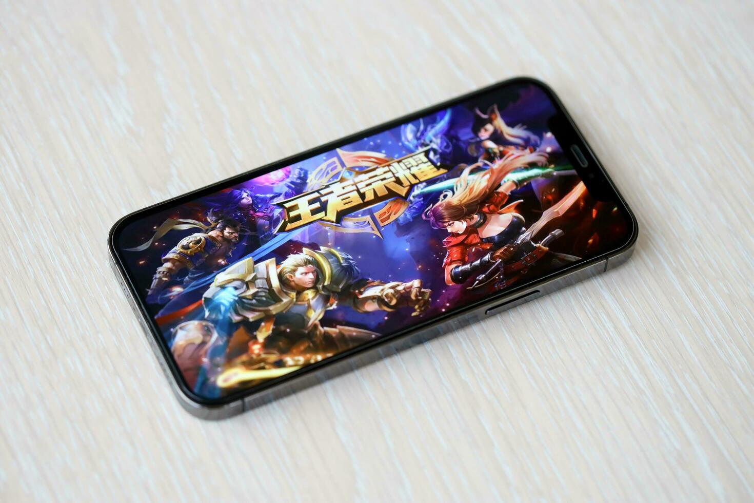 Honor of Kings mobile iOS game on iPhone 15 smartphone screen on wooden table during mobile gameplay photo