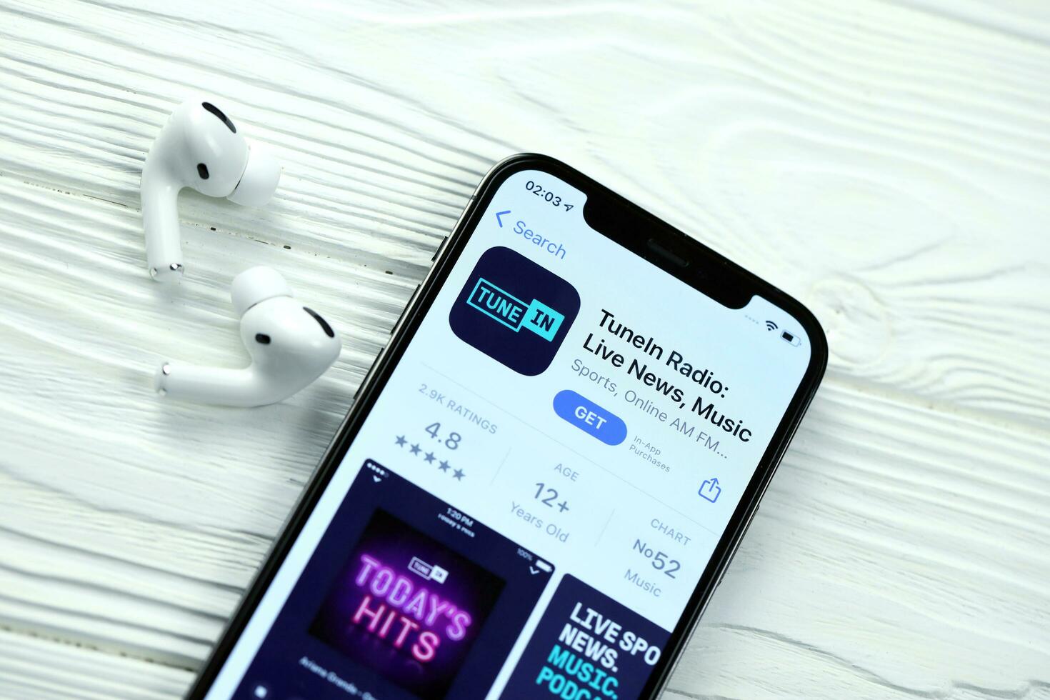 KHARKOV, UKRAINE - MARCH 5, 2021 TuneIn music icon and application from App store on iPhone 12 pro display screen with airpods pro on white table photo