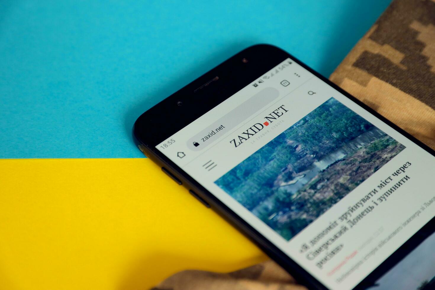 KYIV, UKRAINE - 4 MAY, 2023 Zaxid Net ukrainian news portal on smartphone screen with ukrainian flag and camouflage fabric photo