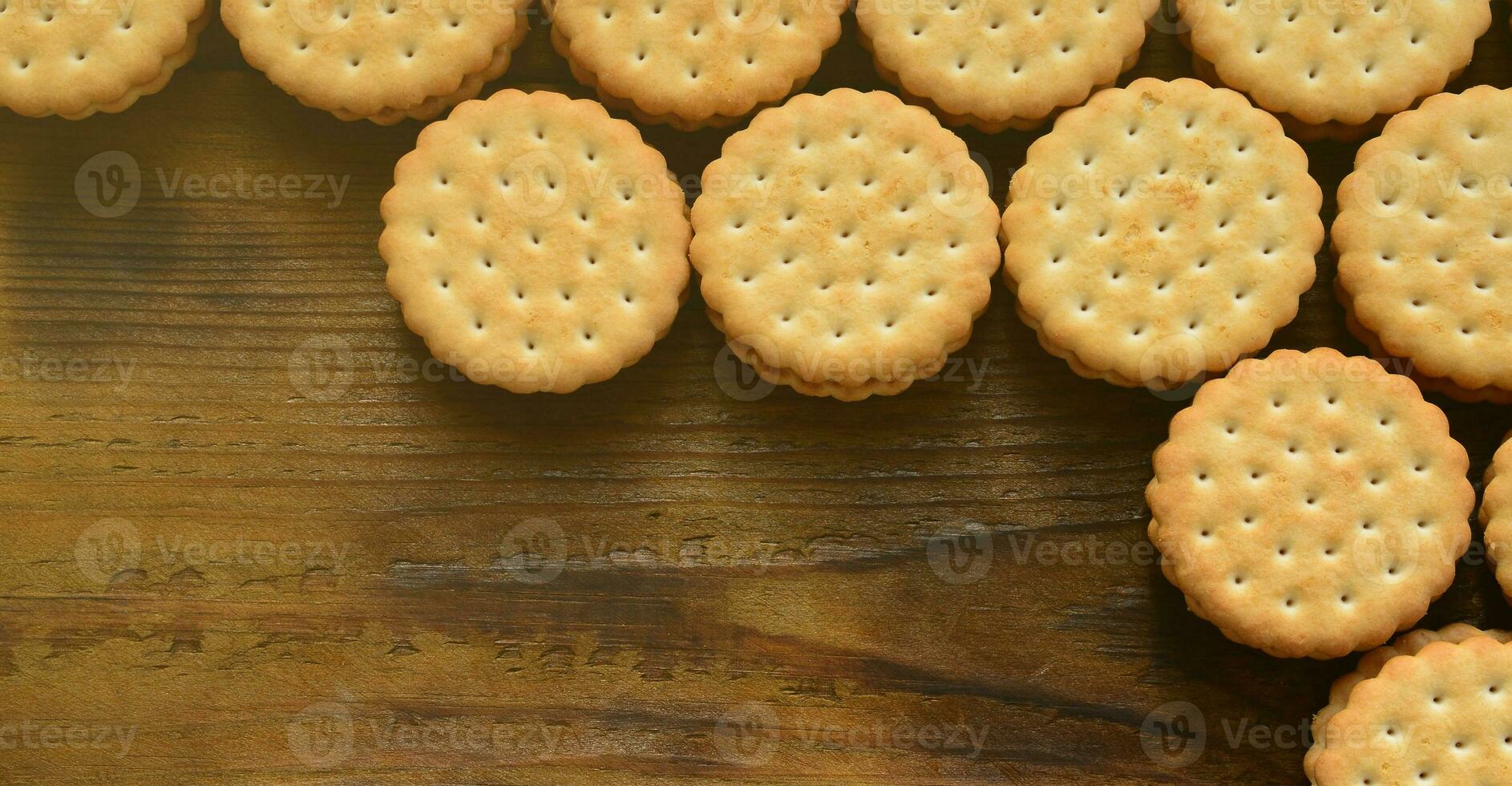 A round sandwich cookie with coconut filling lies in large quantities on a brown wooden surface. Photo of edible treats on a wooden background with copy space