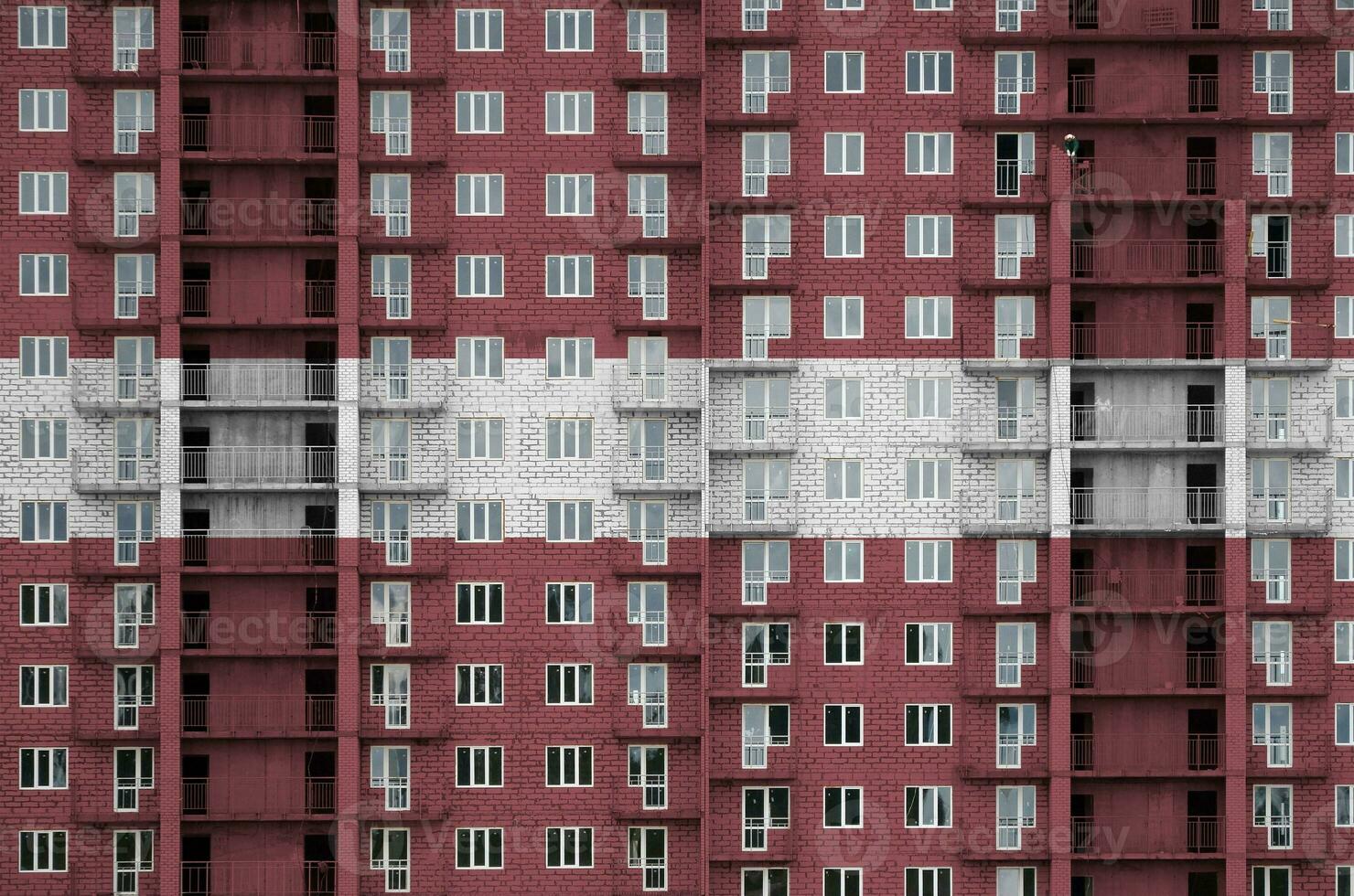 Latvia flag depicted in paint colors on multi-storey residental building under construction. Textured banner on brick wall background photo