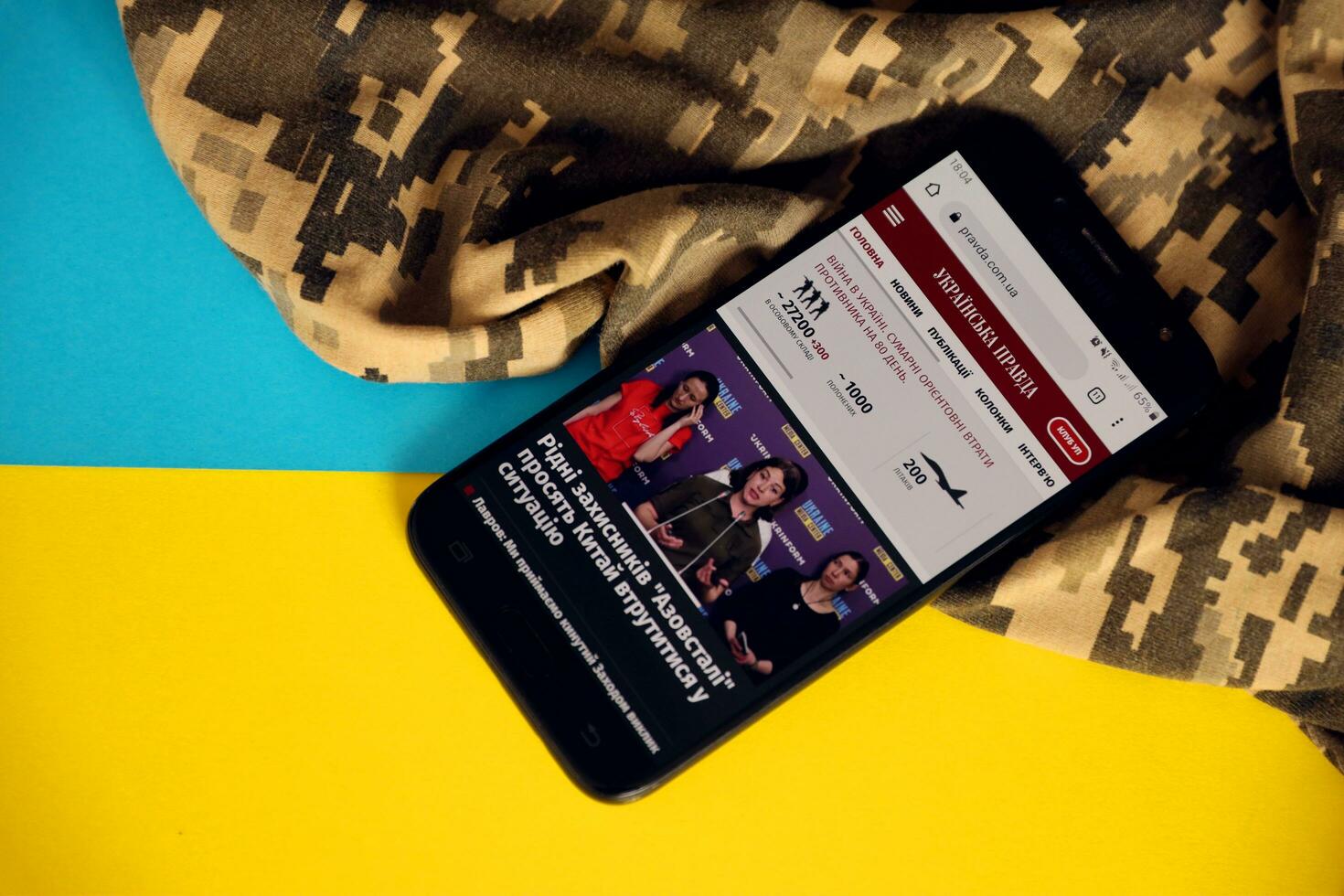 KYIV, UKRAINE - 4 MAY, 2023 UP Ukrainska Pravda ukrainian news portal on smartphone screen with ukrainian flag and camouflage fabric photo