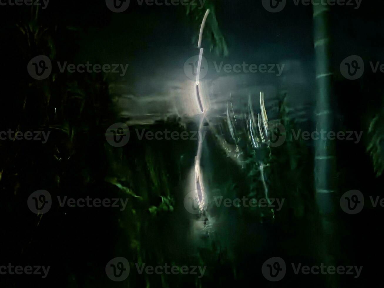 fir trees on meadow between hillsides with conifer forest in fog under the blue sky at night. spooky countryside scenery in full moon light photo