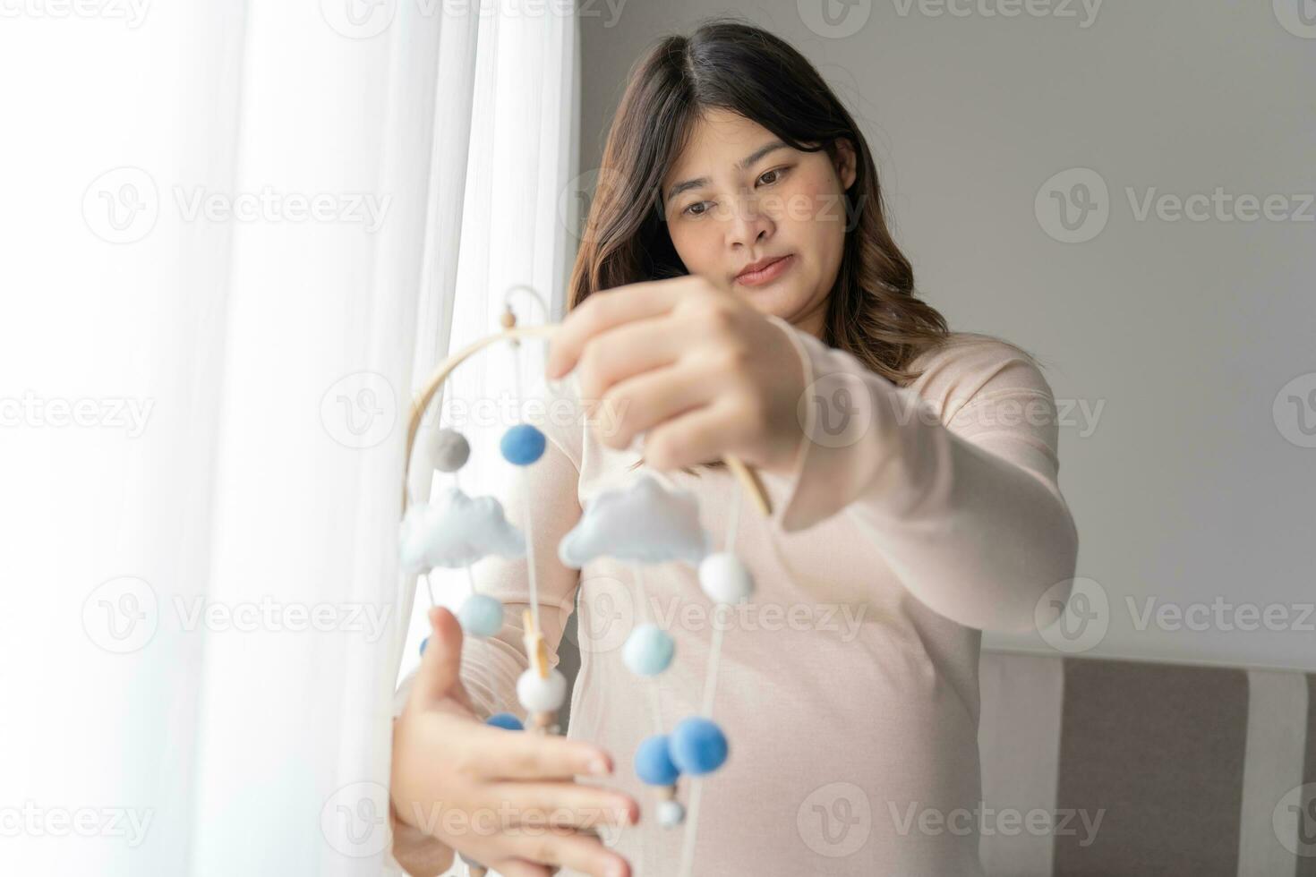 Pregnant asian woman installing baby mobile toy over the baby crib handmade toys above the newborn crib or Baby crib wood mobile photo