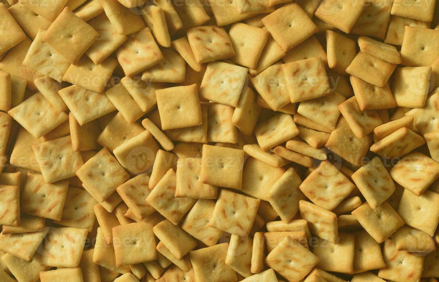 A lot of small cookies are square shaped. A pattern of a yellow salt cracker. Background image with salted pastry photo