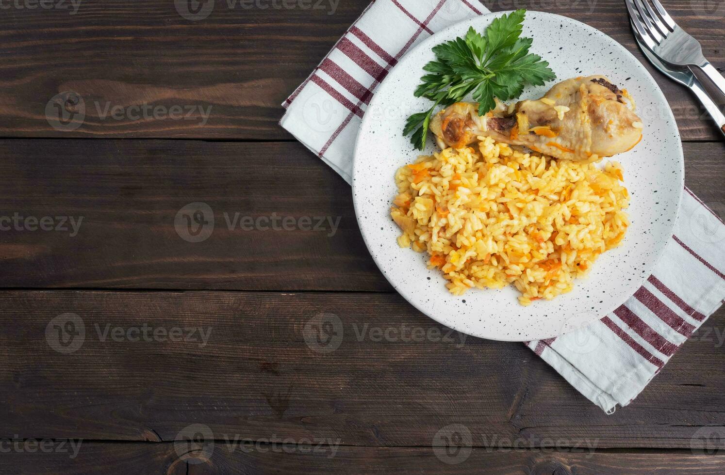 Delicious Asian pilaf, stewed rice with vegetables and chicken drumstick on a plate. Wooden rustic background. Copy space top view photo