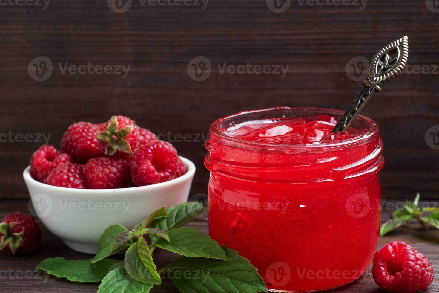 Homemade raspberry jam in a glass jar and fresh raspberries with mint on a wooden rustic background. Copy space photo