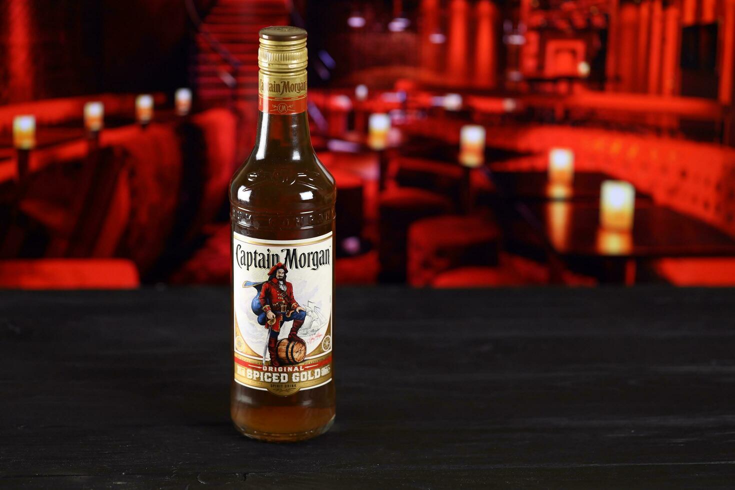 KHARKOV, UKRAINE - FEBRUARY 14, 2021 Captain Morgan original spiced gold spirit drink bottle on wooden table with red bar interior on background. Elite alcohol photo