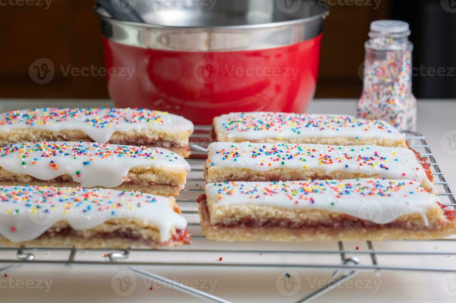 Colorful butter cookies on a kitchen counter with a red mixing bowl and a bottle of sprinkles in the background. photo