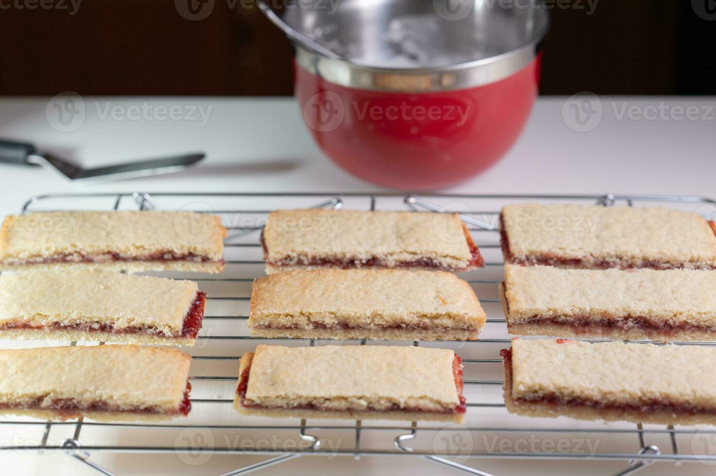 Shortbread cookies and a red mixing bowl of icing on the counter in the background. photo