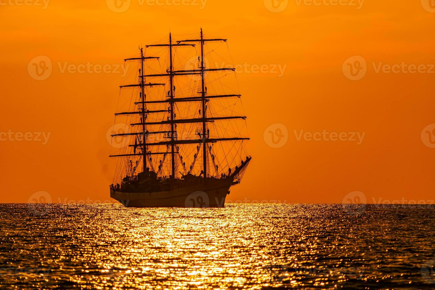 A red burning sunset with the silhouette of sailing ship. Sailors set sails on masts of ship. White sailing vessel floating in the sea. Copy space. photo