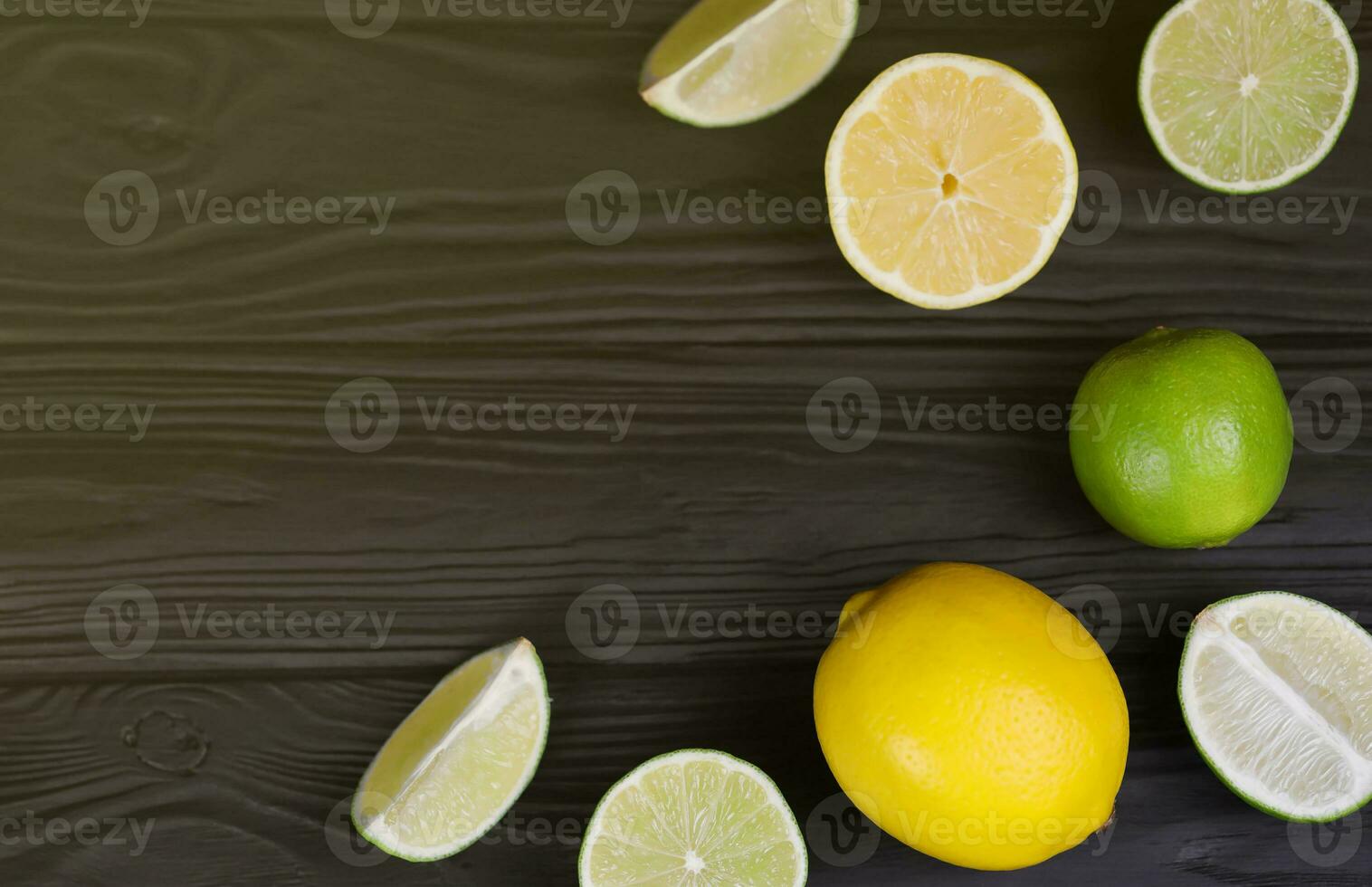 Many halves and slices of yellow lemon and green lime on black wooden table. Fresh fruits on kitchen top with copy space for text photo