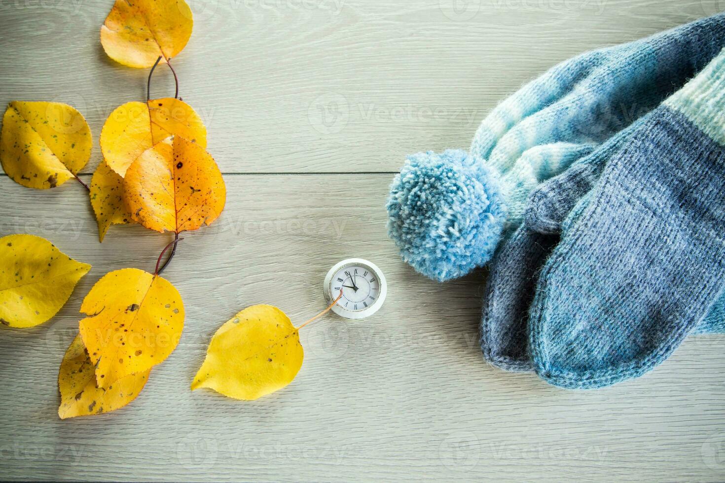 Autumn foliage, winter mittens and a clock on a wooden table. photo