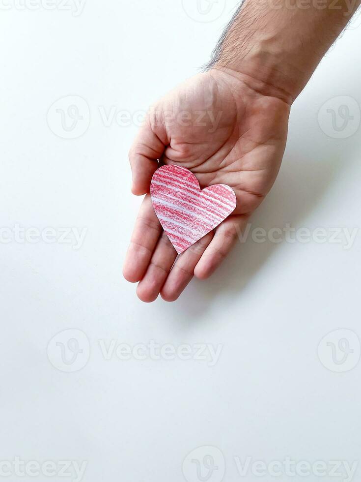 A mans hand holds a red paper heart on a white background. Empty space for an inscription. The photo