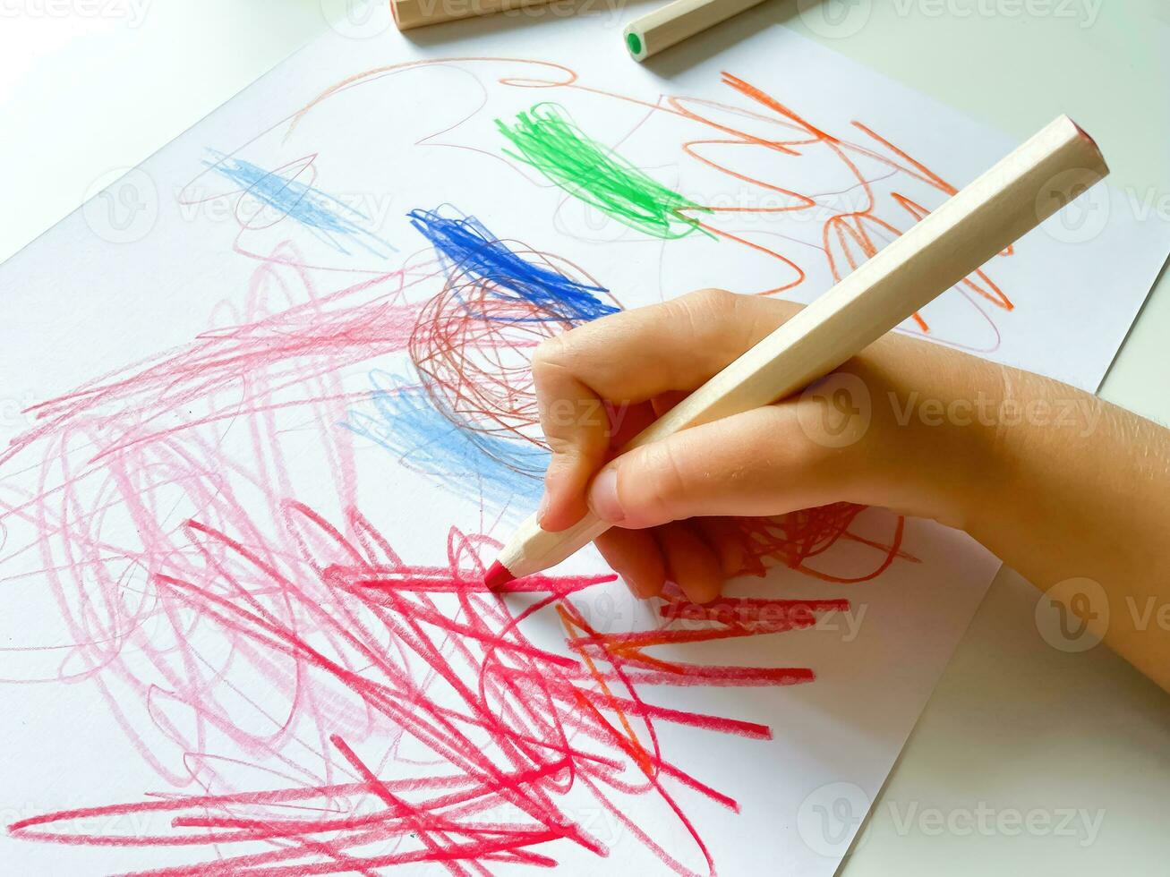 pequeño niño sorteos con de colores lapices en papel en blanco mesa. foto