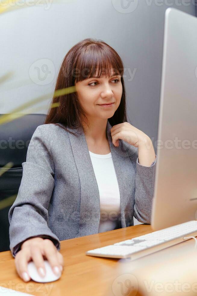 A brunette woman at a computer in the workplace. Business concept. photo