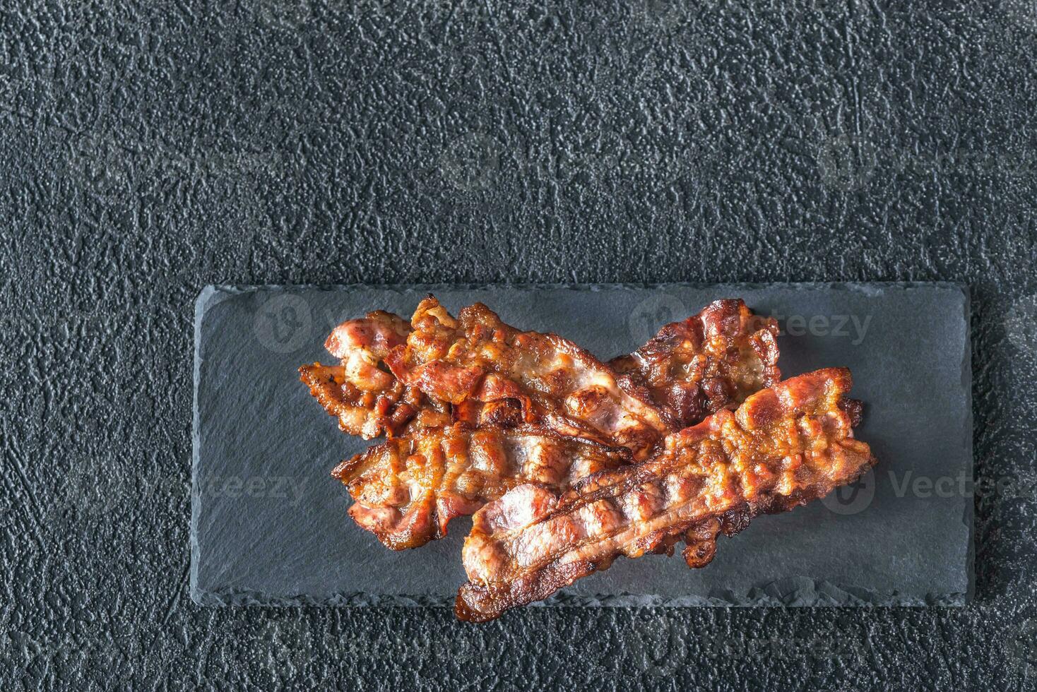 Fried bacon strips on the stone dark board photo