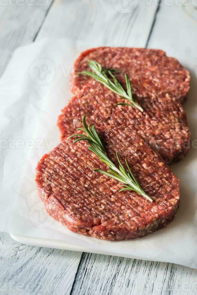 Raw beef patties on the white parchment photo