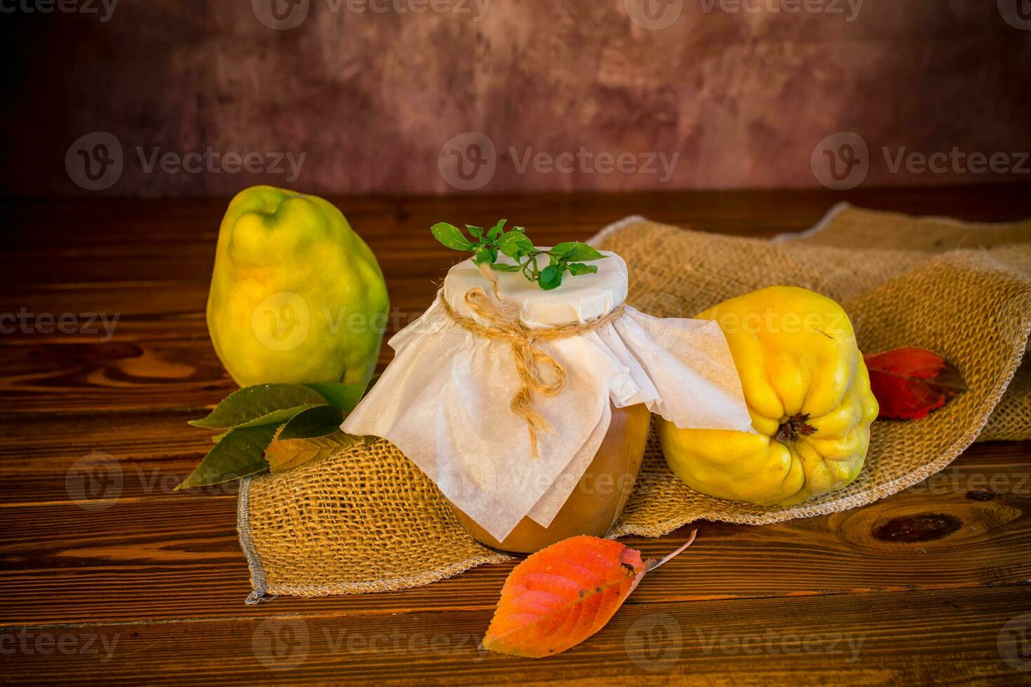 Ripe quince fruits with jam in a glass jar on a dark wooden table. photo