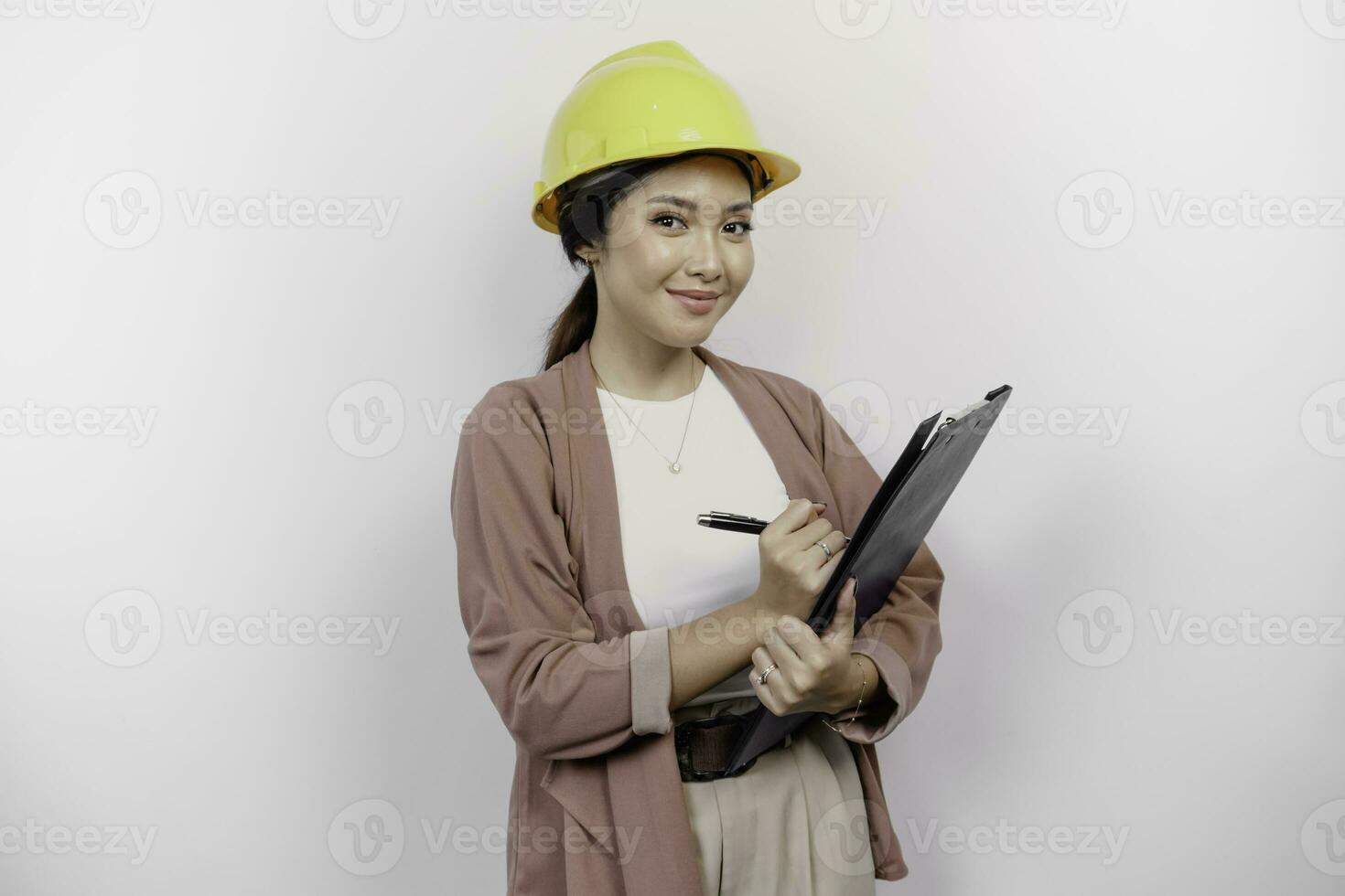 Smiling young Asian woman employee wearing safety helmet while holding a clipboard, isolated by white background photo