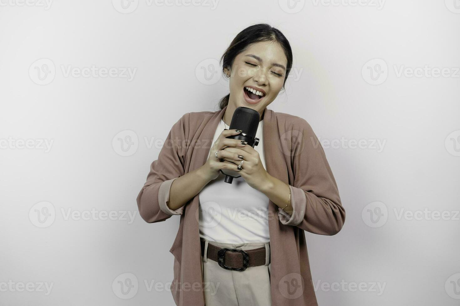 despreocupado asiático mujer es teniendo divertido karaoke, canto en micrófono mientras en pie terminado blanco antecedentes foto