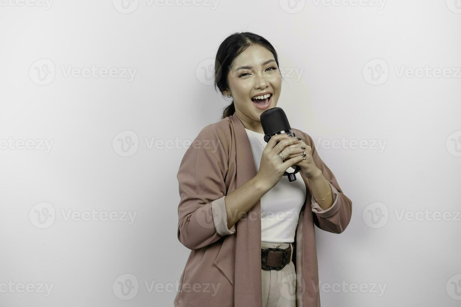 Carefree Asian woman is having fun karaoke, singing in microphone while standing over white background photo