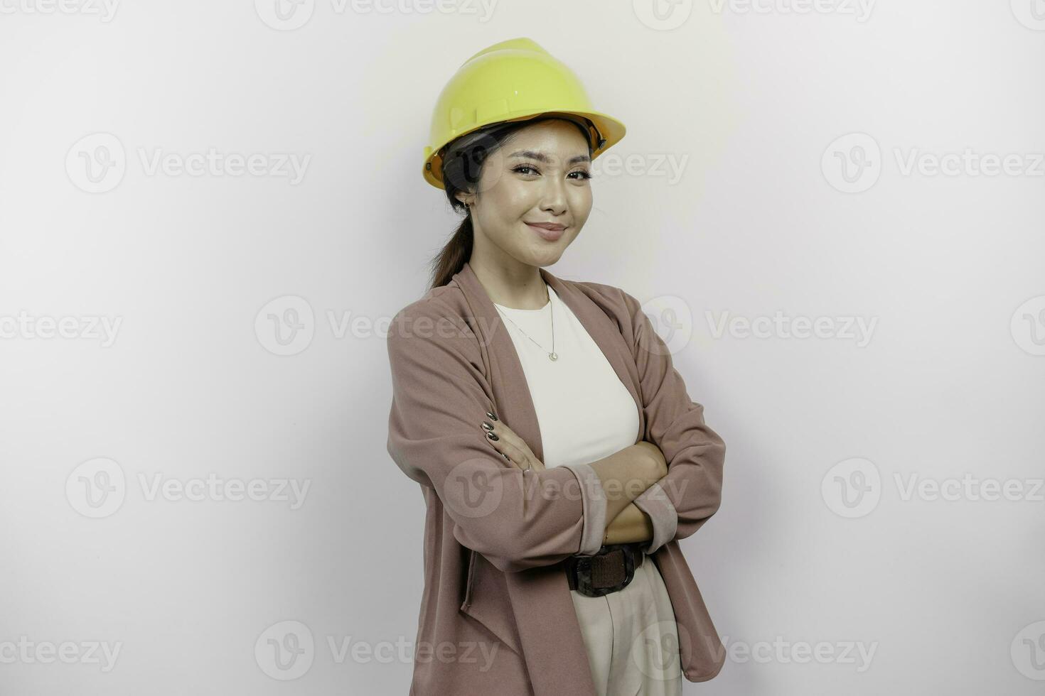 un confidente sonriente asiático mujer empleado vistiendo la seguridad casco en pie con brazos doblada y mirando a el cámara aislado terminado blanco antecedentes foto