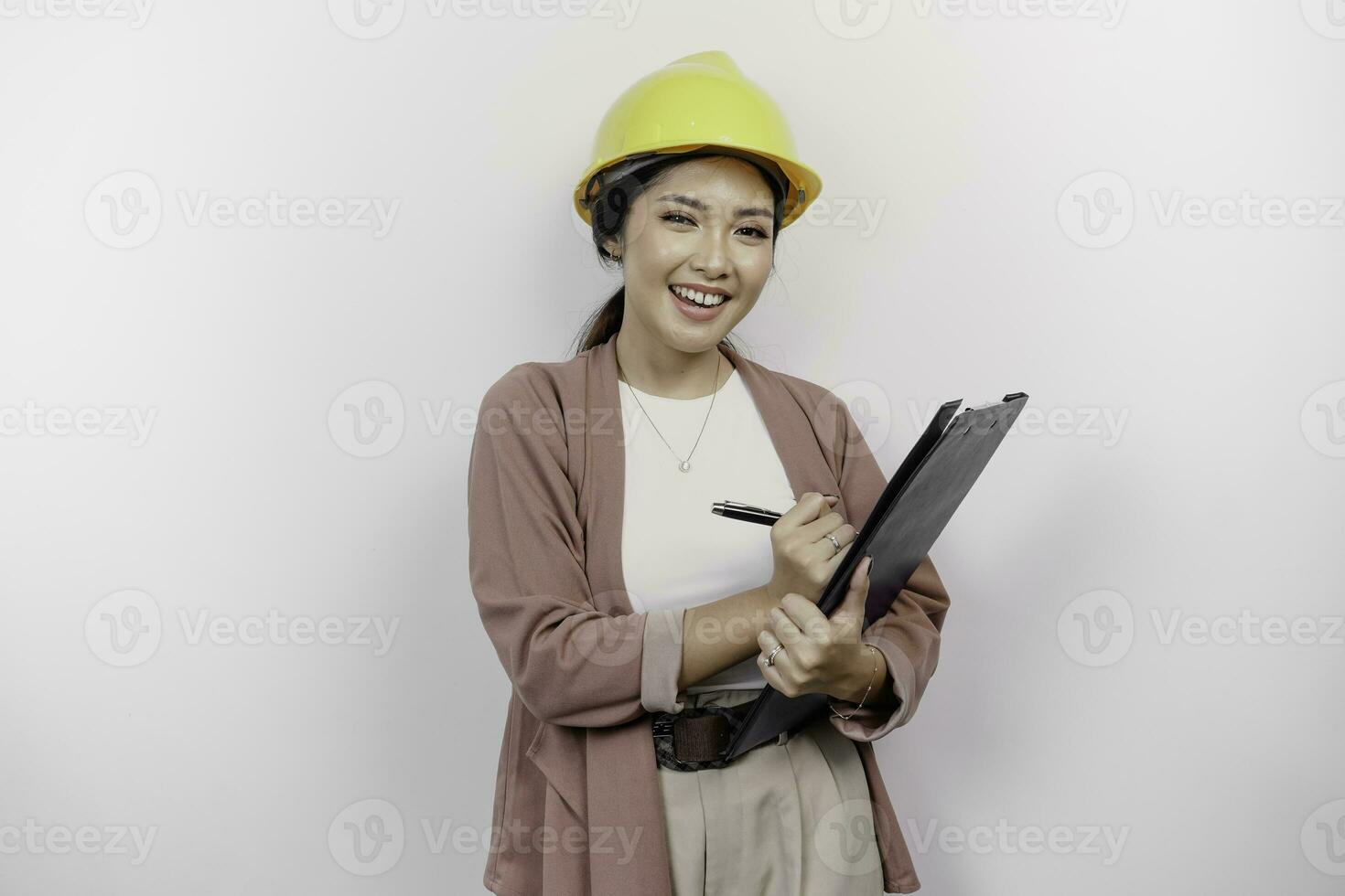 sonriente joven asiático mujer empleado vistiendo la seguridad casco mientras participación un portapapeles, aislado por blanco antecedentes foto