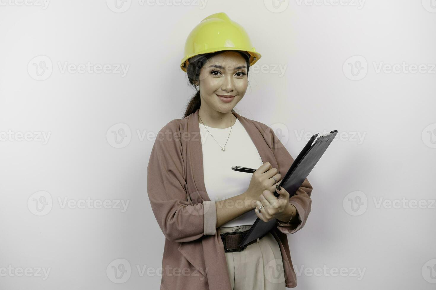 Smiling young Asian woman employee wearing safety helmet while holding a clipboard, isolated by white background photo