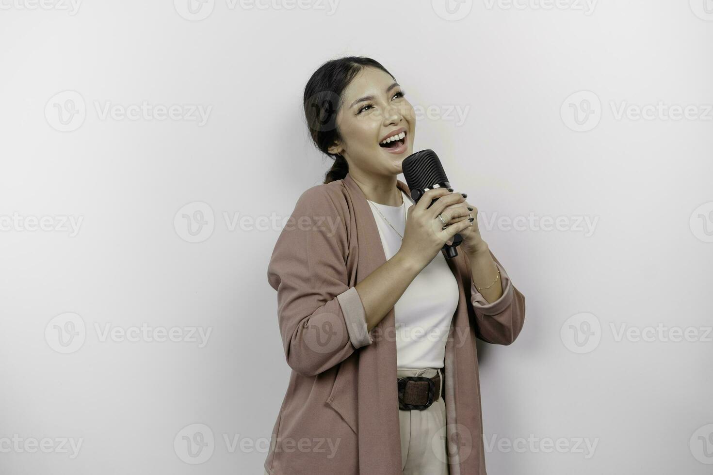 despreocupado asiático mujer es teniendo divertido karaoke, canto en micrófono mientras en pie terminado blanco antecedentes foto