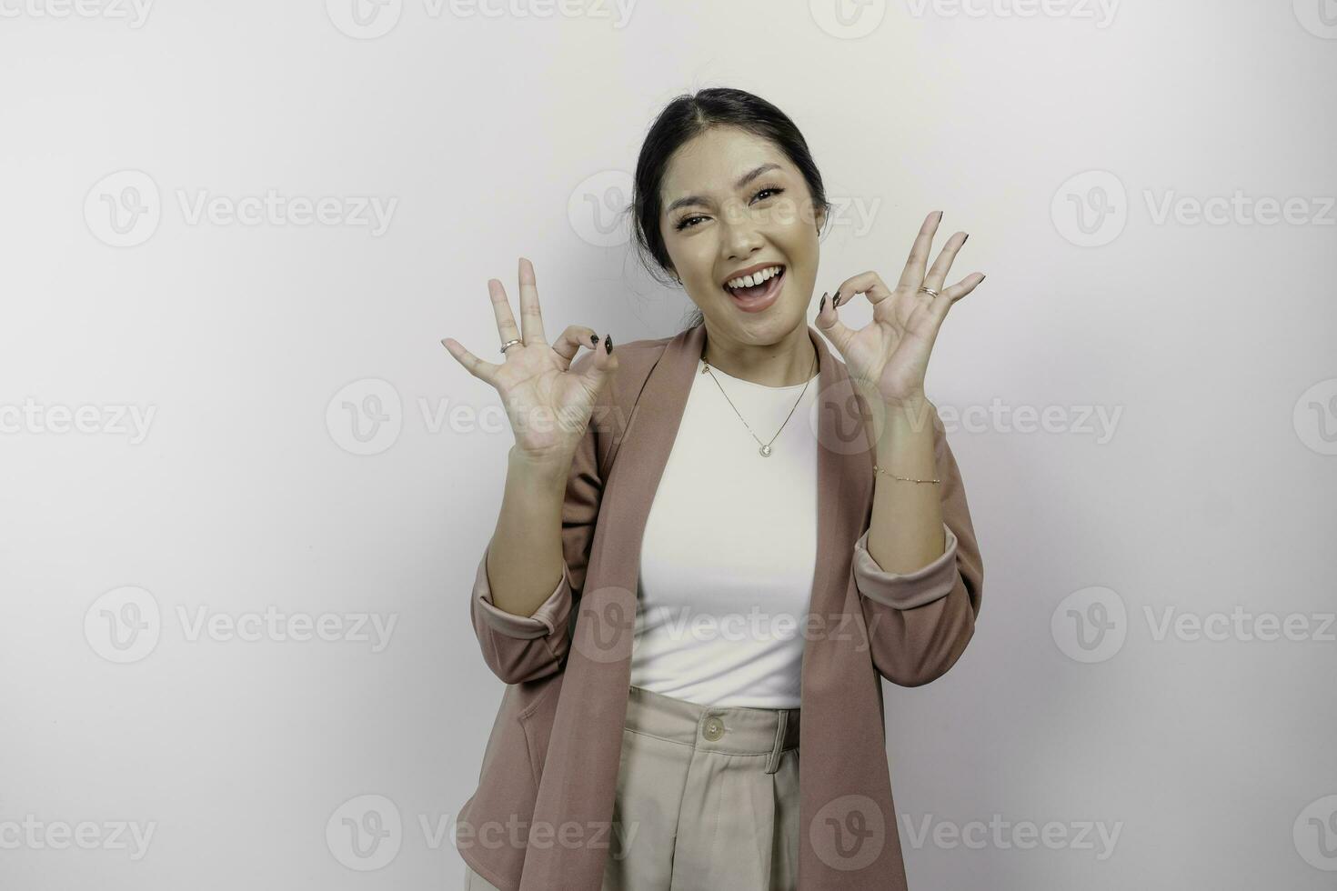 emocionado asiático mujer empleado vistiendo un cárdigan dando un Okay mano gesto aislado por un blanco antecedentes foto