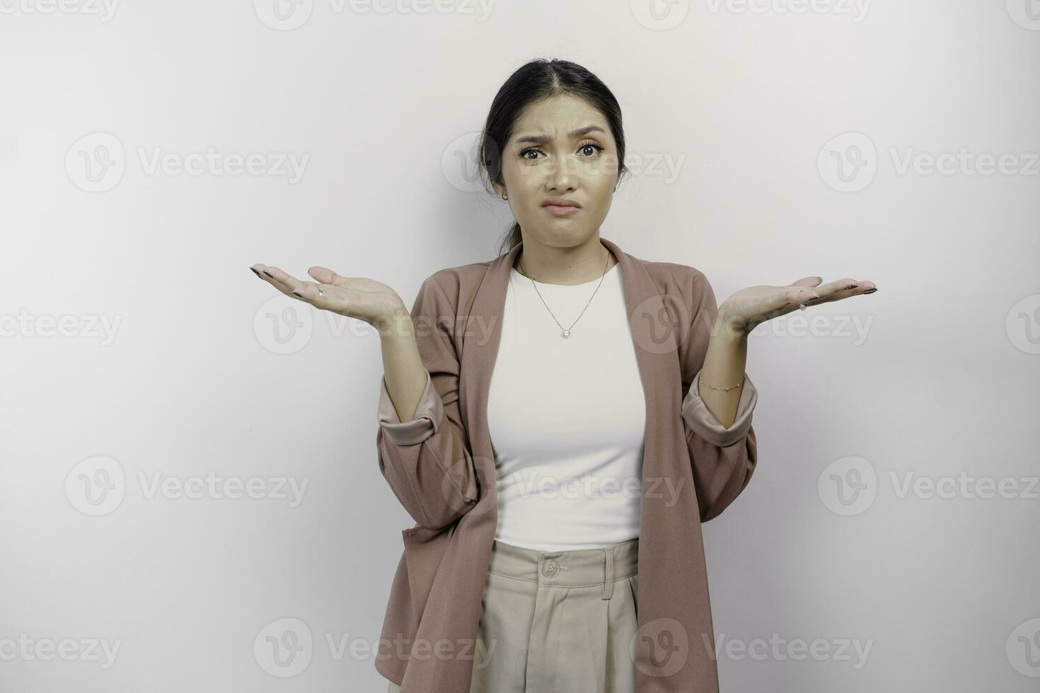 An Asian woman employee wearing a cardigan looks so confused between choices, isolated by a white background photo