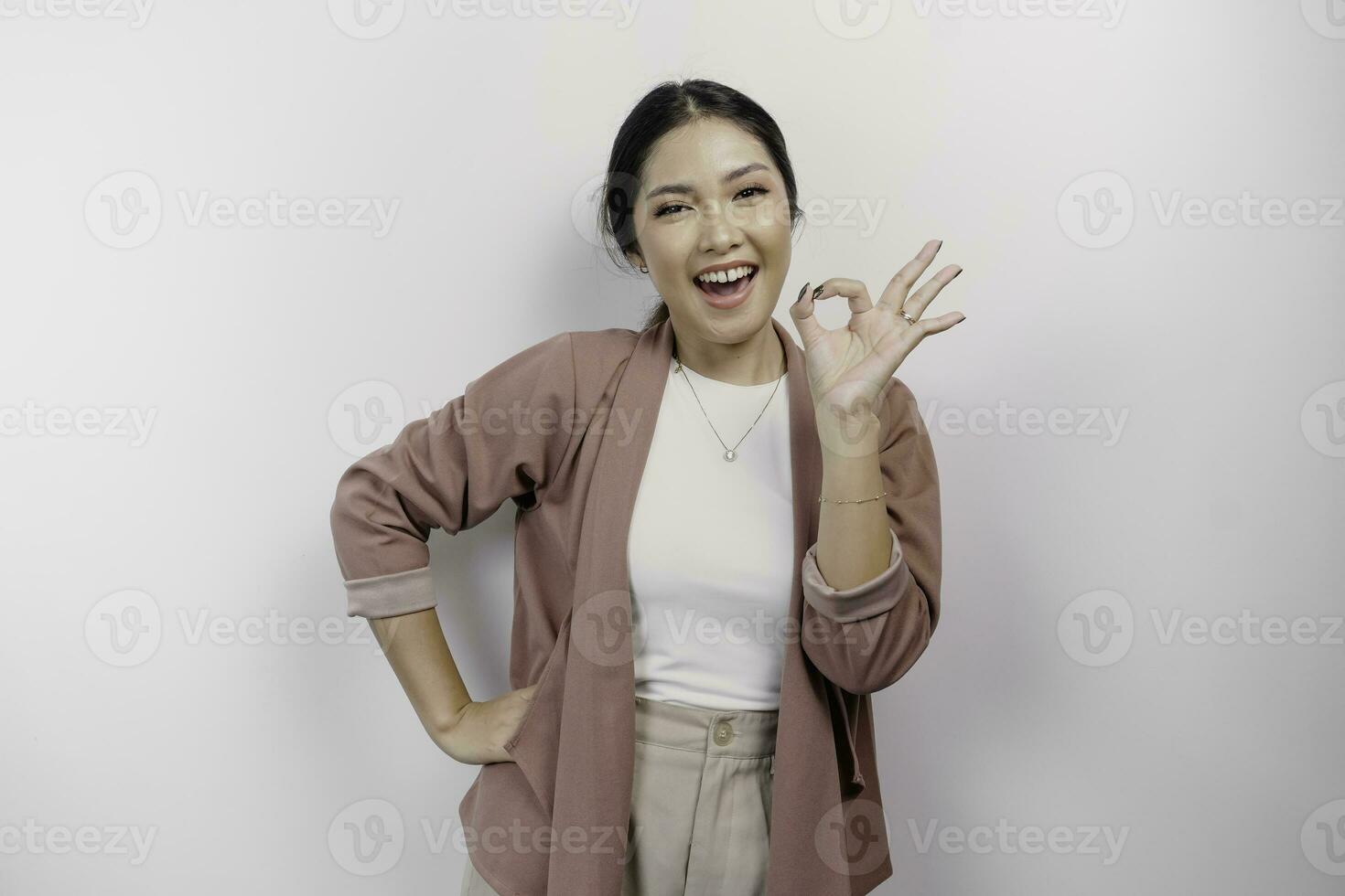 Excited Asian woman employee wearing a cardigan giving an OK hand gesture isolated by a white background photo