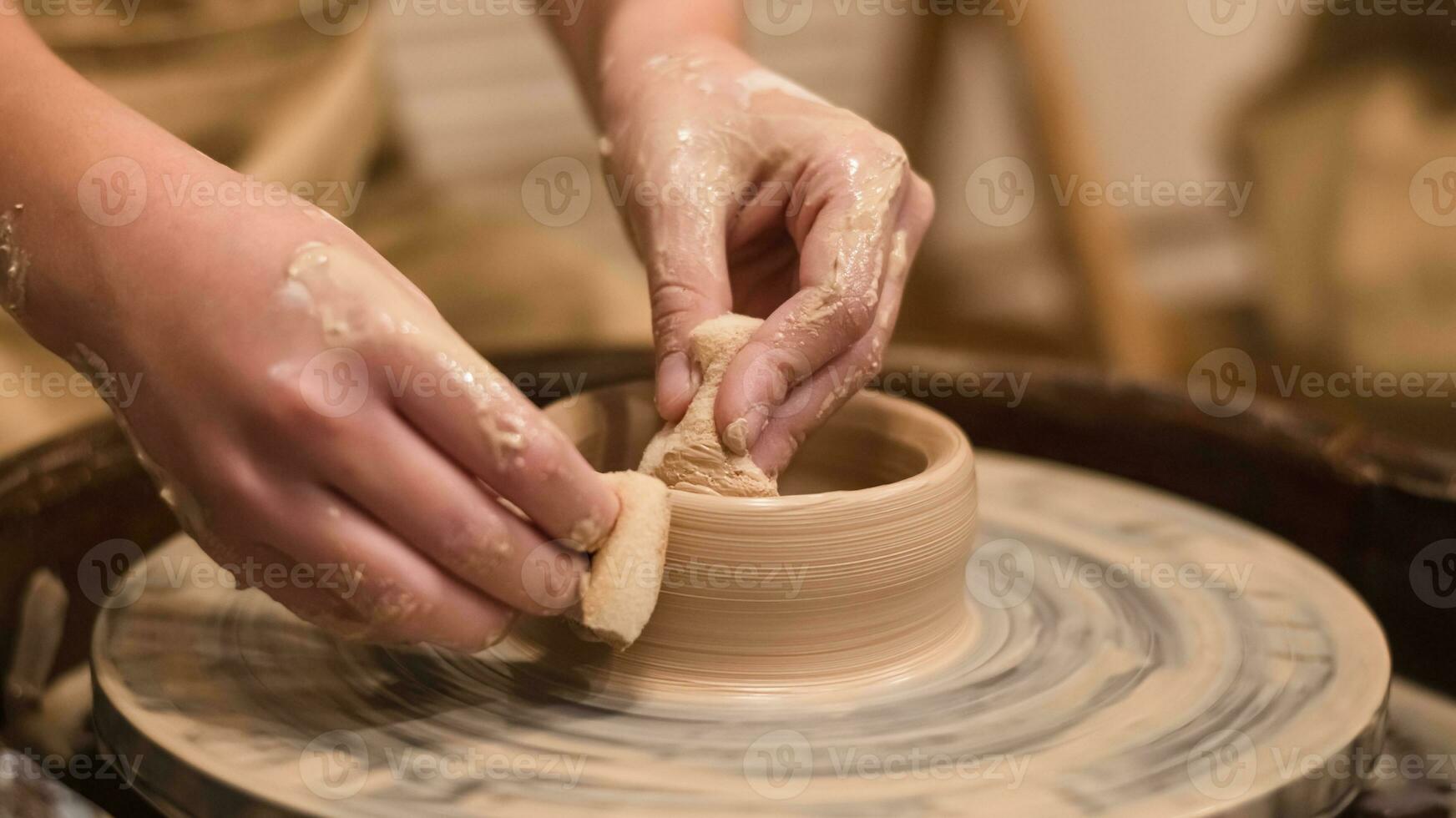 Potter girl works on potter's wheel, making ceramic pot out of clay in pottery workshop photo