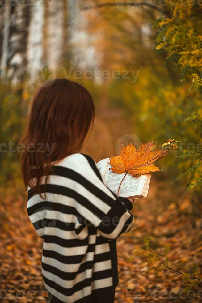 niña con pecas con un libro entre otoño hojas foto