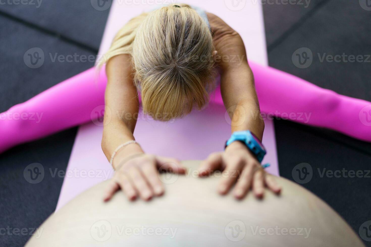 Unrecognizable woman doing stretching exercise with fitness ball in gym on mat photo
